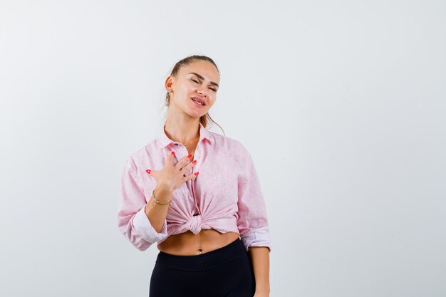 Jeune femme gardant la main sur la poitrine en chemise, pantalon et à la reconnaissance. vue de face.