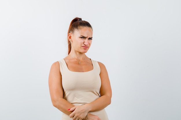 Jeune femme gardant les mains devant elle en débardeur et à la dégoûté, vue de face.