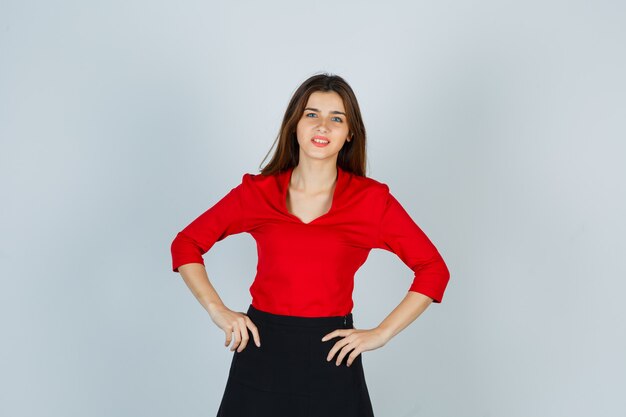 Jeune femme gardant les mains sur la hanche en chemisier rouge, jupe et magnifique