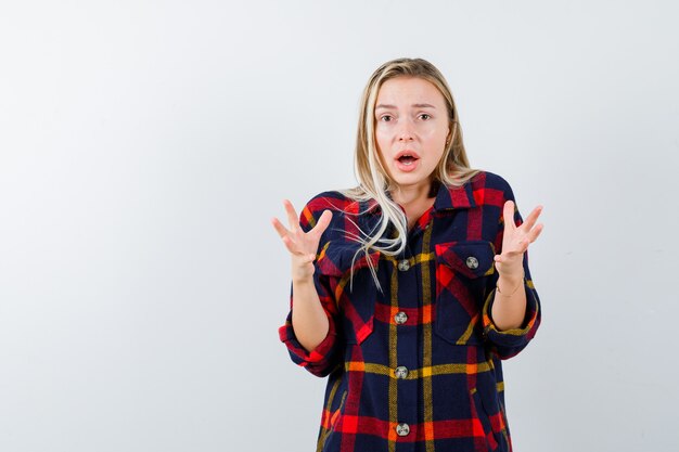 Jeune femme en gardant les mains de manière agressive en chemise à carreaux et à la vue ennuyée, de face.