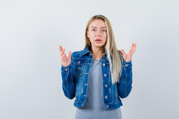 Jeune femme gardant les mains de manière agressive en t-shirt, veste en jean, jupe et l'air en colère.