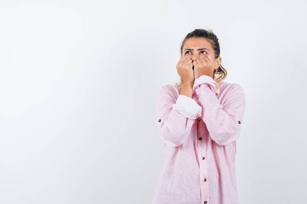 Jeune femme en gardant les poings sur la bouche en chemise rose et à la peur