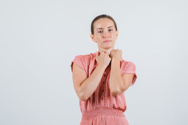 Jeune femme gardant les poings sur le col en robe rayée, vue de face.