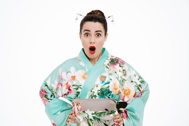 jeune femme geisha en kimono japonais traditionnel regardant à l'avant avec la bouche grande ouverte et les yeux étonnés et surpris debout sur un mur blanc