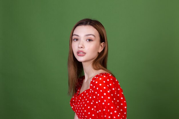 Jeune femme avec de grandes lèvres brunes de maquillage naturel parfait en robe rouge à pois sur un mur vert posant