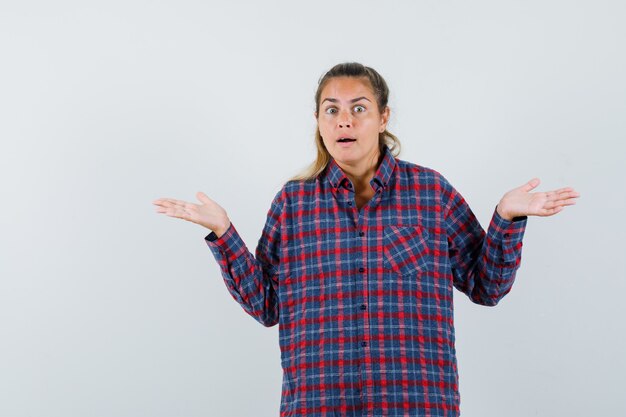 Jeune femme en haussant les épaules en chemise à carreaux et à la perplexité