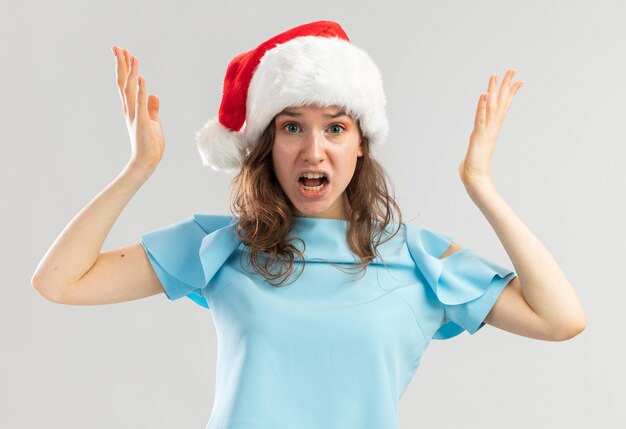 Jeune femme en haut bleu et bonnet de Noel à la recherche de crier avec une expression ennuyée d'être frustré