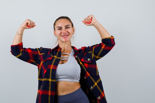 Jeune femme en haut, chemise à carreaux montrant le geste du gagnant et semblant chanceuse, vue de face.