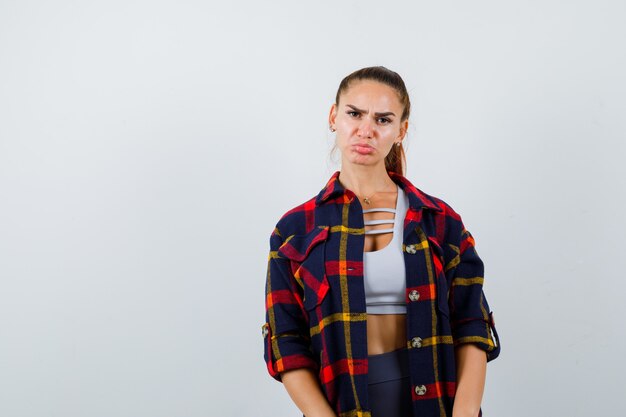 Jeune femme en haut court, chemise à carreaux, lèvres boudeuses et l'air offensé, vue de face.