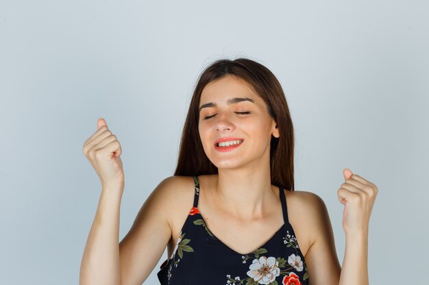 Jeune femme en haut floral montrant le geste du gagnant et l'air heureux