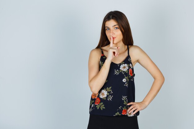 Jeune femme en haut floral montrant le geste de silence