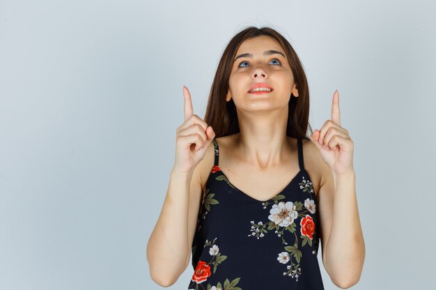 Jeune femme en haut floral pointant vers le haut et à la rêveuse