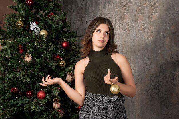 Jeune femme en haut noir tenant des boules brillantes dans une chambre décorée de Noël