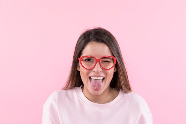 Jeune femme heureuse avec des lunettes montrant la langue