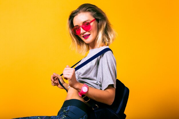 Jeune femme heureuse portant une tenue sportive décontractée, un sac à dos et des lunettes néon