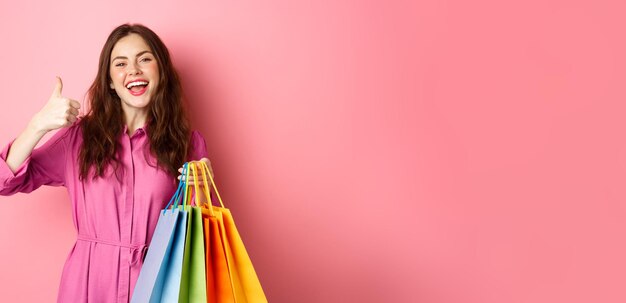 Jeune femme heureuse shopper montrant les pouces vers le haut heureux avec de bonnes remises achetant du personnel en vente holdin