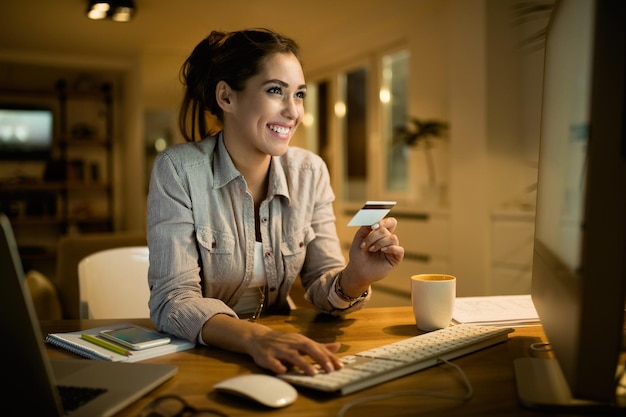 Photo gratuite jeune femme heureuse utilisant une carte de crédit pour faire des achats en ligne le soir à la maison