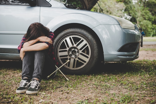Jeune femme hipster en attente d&#39;une assistance routière après que sa voiture se décompose sur le côté de la route assise contre sa voiture.