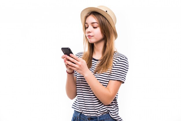 Jeune femme hipster en chapeau de paille et lunettes de soleil à l'aide de téléphone portable sur mur blanc