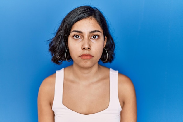 Photo gratuite jeune femme hispanique debout sur fond bleu détendu avec une expression sérieuse sur le visage simple et naturel en regardant la caméra