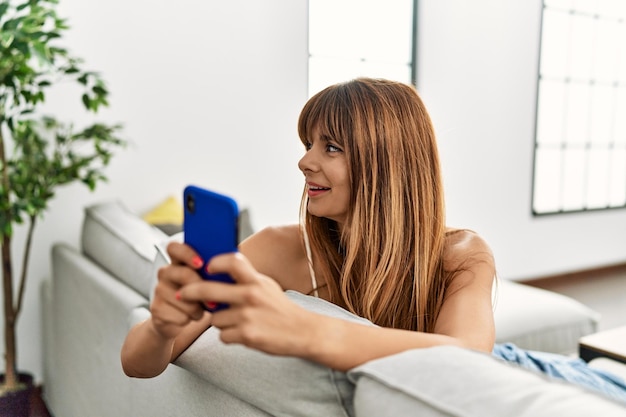 Jeune femme hispanique souriante confiante utilisant un smartphone à la maison