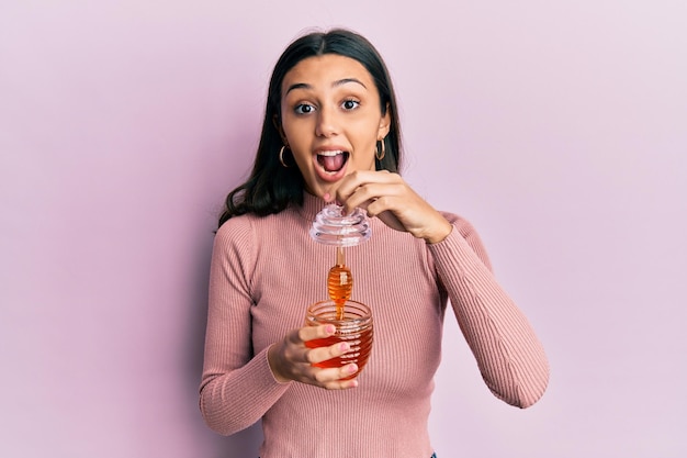 Photo gratuite jeune femme hispanique tenant du miel célébrant la folie et étonnée du succès avec les yeux ouverts hurlant d'excitation