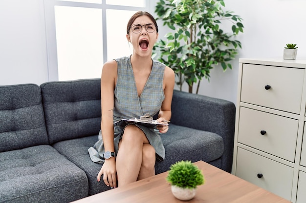 Photo gratuite jeune femme hispanique travaillant à la clinique de psychologie en colère et folle criant frustré et furieux criant avec colère rage et concept agressif