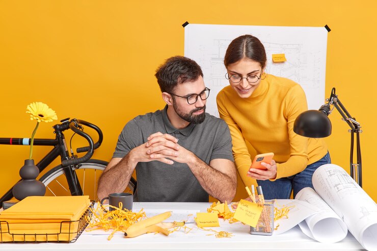 Photo gratuit une jeune femme et un homme professionnels satisfaits des employés de bureau collaborent pendant le travail d'équipe sur des plans à la recherche d'idées sur internet concentrés sur un téléphone portable moderne discutent d'idées de projet