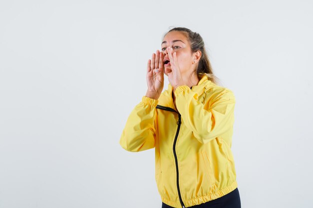 Jeune femme en imperméable jaune appelant quelqu'un avec une voix forte