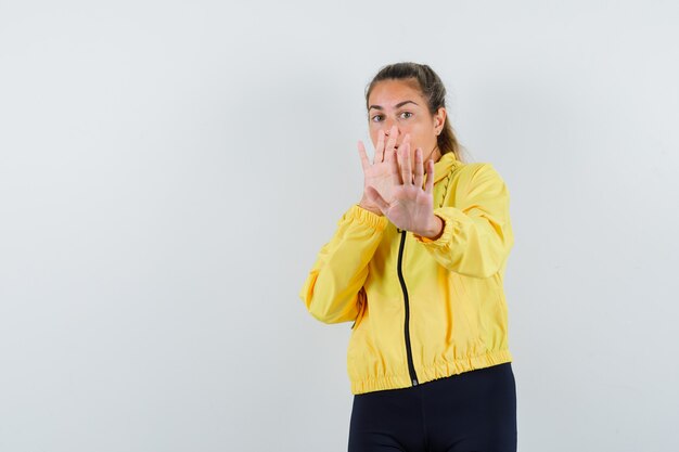 Jeune femme en imperméable jaune levant les mains se défendre et à la troublé