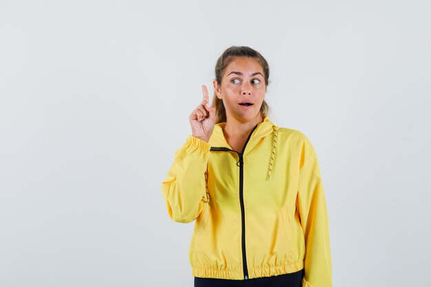 Jeune femme en imperméable jaune pointant vers le haut tout en regardant de côté et à la prudence