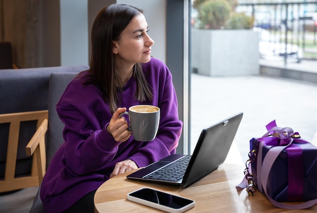 Photo gratuite une jeune femme indépendante dans un café avec une tasse de café et un coffret cadeau