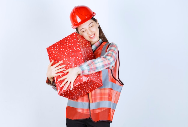 Jeune femme ingénieur en casque rouge étreint la boîte-cadeau.