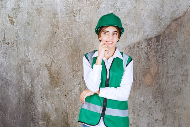 Jeune femme ingénieur en gilet vert et casque debout et posant