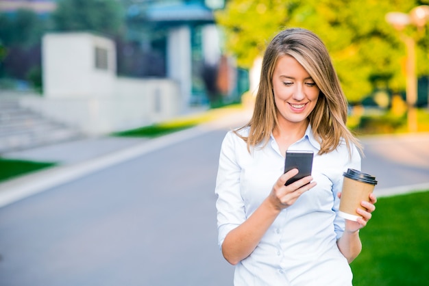 Jeune femme intelligente professionnelle en utilisant un téléphone. Une femme d&#39;affaires en train de lire des nouvelles ou des SMS sms sur un téléphone intelligent tout en buvant du café en rupture de travail.