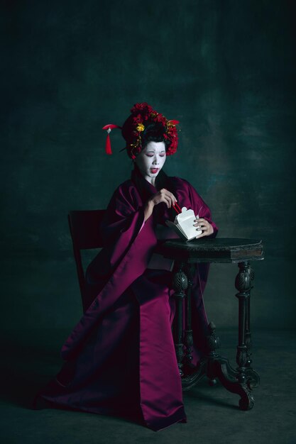 Jeune femme japonaise comme geisha sur fond vert foncé. Style rétro, concept de comparaison des époques.