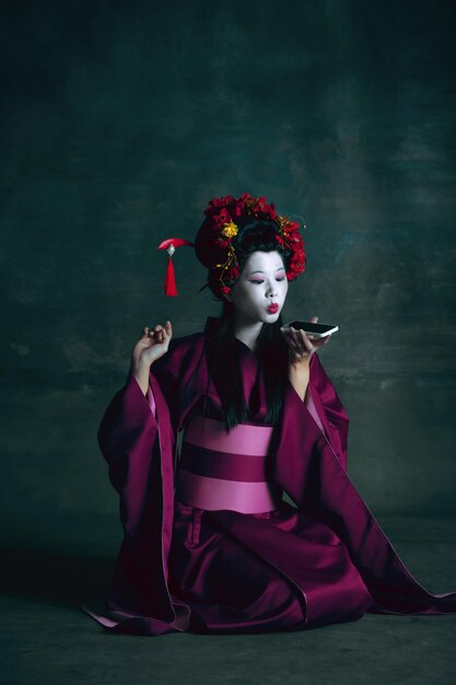 Jeune femme japonaise comme geisha sur vert foncé. Style rétro, concept de comparaison des époques.