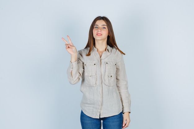 Jeune Femme En Jeans Décontractés Montrant Le Geste De La Victoire Et L'air Heureux, Vue De Face.