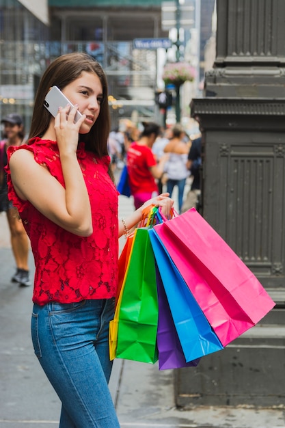 Photo gratuite jeune femme en jeans téléphonant avec des sacs à provisions