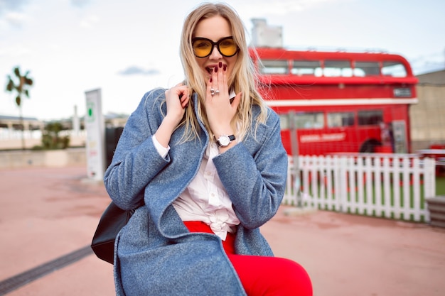 Jeune femme jolie blonde posant dans la rue, portant manteau et sac à dos à la mode, style étudiant hipster, s'amuser et sourire, joli visage positif.