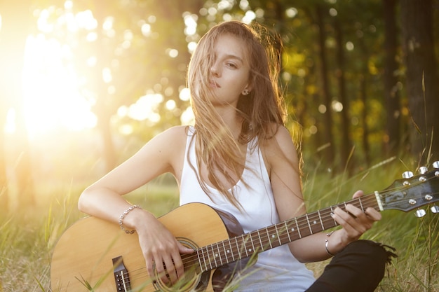 Jeune femme jouant de la guitare dans la nature pendant le coucher du soleil