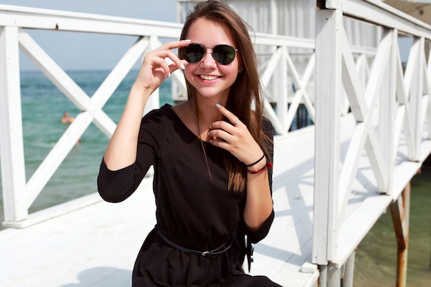 Jeune femme jouant avec ses lunettes de soleil et assis sur la jetée