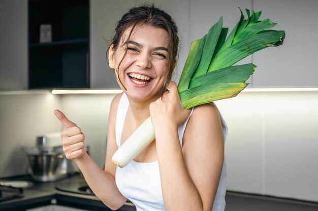 Une jeune femme joyeuse dans la cuisine tient un poireau dans ses mains