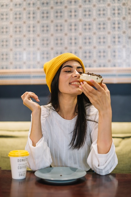 Photo gratuite jeune femme joyeuse avec dessert près de tasse à table dans un café