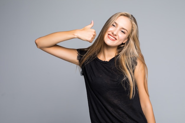 Jeune femme joyeuse heureuse montrant le pouce vers le haut isolé sur fond gris