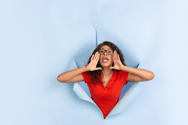 Une jeune femme joyeuse pose dans un trou de papier bleu déchiré, émotionnel et expressif