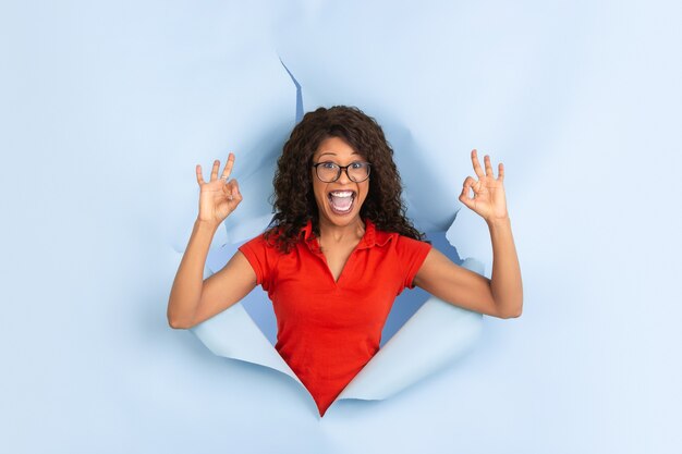 Une jeune femme joyeuse pose dans un trou de papier bleu déchiré, émotionnel et expressif