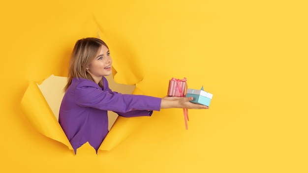 Une jeune femme joyeuse pose dans un trou de papier jaune déchiré, émotionnel et expressif