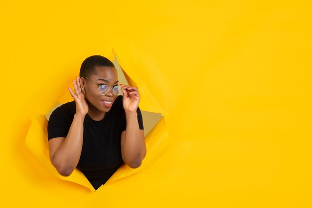 Une jeune femme joyeuse pose dans un trou de papier jaune déchiré