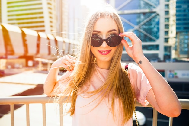 Une jeune femme joyeuse regarde ses lunettes de soleil posant sous la